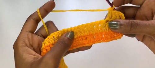 Hands holding a small crocheted swatch in orange and yellow showing the stitch texture in progress
