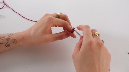 Hands holding a crochet hook and working the first stitches with dark red yarn on a white surface