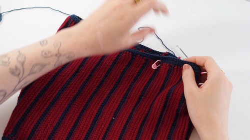 Hands pinning the navy border edge onto a completed ribbed crochet panel in burgundy and navy stripes