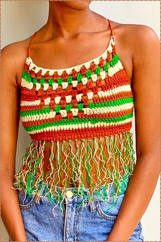 Finished crochet fringe top worn with denim shorts showing rust brown green and cream stripes granny stitch detailing and long multicolor fringe along the hem 