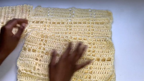 Hands smoothing out two flat crocheted panels in pale yellow showing an open mesh grid stitch texture ready for assembly
